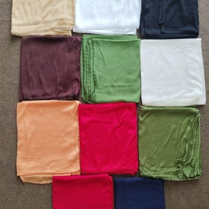 Puede incluir: Colección de pañuelos cuadrados plegados en varios colores, incluyendo beige, blanco, azul marino, burdeos, verde, naranja y rojo. Cada pañuelo tiene un delicado ribete de encaje. Los pañuelos están cuidadosamente dispuestos sobre una superficie neutra.