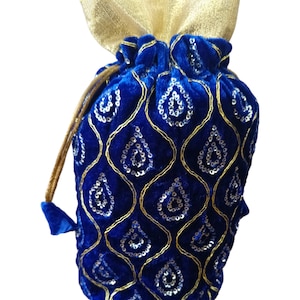 Puede incluir: Una bolsa de terciopelo azul real con una parte superior dorada y brillante. La bolsa está adornada con un patrón dorado en forma de lágrima lleno de lentejuelas plateadas. El cordón es de color dorado.
