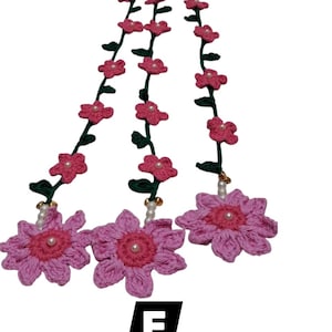 May include: A crochet garland featuring three large pink flowers with dark pink centers and white pearl accents, connected by green vines adorned with smaller pink flowers. The letter F is displayed in a black square at the bottom of the image.