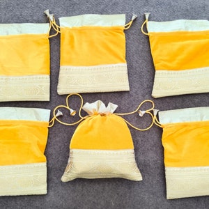 May include: Six yellow velvet drawstring bags with gold trim. The bags have a white lining and are tied with a yellow cord.