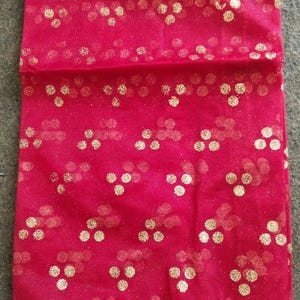 Peut inclure: Un tissu rouge transparent avec des points de paillettes dorées et une bordure en dentelle dorée. Le tissu est plié en deux.