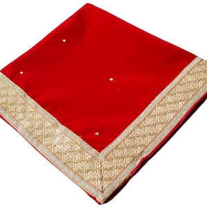 Puede incluir: Un textil rojo vibrante con un borde bordado en oro ornamentado. La tela cuadrada tiene una textura suave y está adornada con pequeños adornos brillantes. El borde dorado presenta un patrón geométrico, agregando un toque de elegancia al diseño.