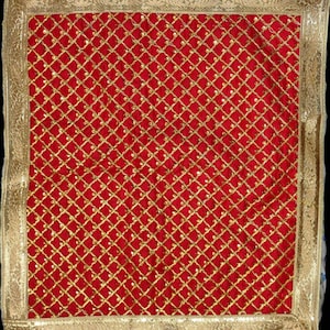 May include: A red velvet square with a gold embroidered grid pattern. The grid is made of small gold circles and lines. The square has a gold border.