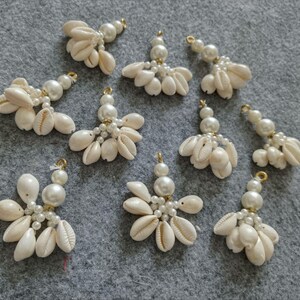 May include: Ten white shell and pearl charms with gold accents. Each charm features a cluster of small white shells and pearls.