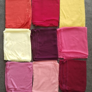 Puede incluir: Nueve pañuelos coloridos en tonos de rojo, rosa y amarillo, dispuestos en una cuadrícula. Cada pañuelo está doblado y tiene un borde festoneado. Los pañuelos están hechos de tela ligera.