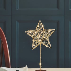 Könnte beinhalten: Ein goldener Stern aus Draht mit warmweißen LED-Lichtern auf einem goldenen Ständer. Der Stern ist eine dekorative Leuchte für eine Tischplatte.