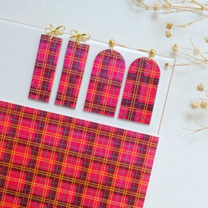 Op de afbeelding: Vier paar rode en zwarte geruite oorbellen met gouden accenten. De oorbellen worden getoond op een wit oppervlak met een rood en zwart geruit patroon.