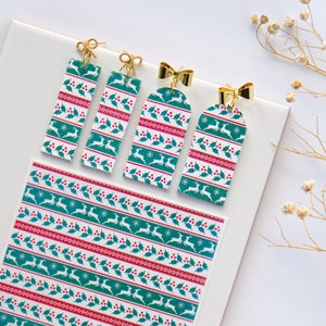 May include: Four Christmas-themed earrings with a white background and green and red patterns. The earrings are shaped like rectangular tags with a gold bow at the top. The pattern features a repeating design of holly leaves, red berries, and reindeer.