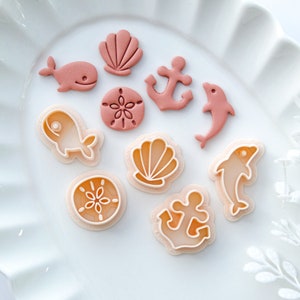 May include: A set of ten pink plastic cookie cutters shaped like seashells, anchors, dolphins, and starfish.