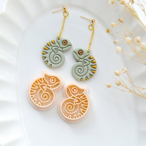 May include: A pair of green chameleon earrings with gold accents and a pair of pink chameleon cookie cutters.