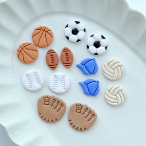 Pu&ograve; includere: Una collezione di 12 orecchini in argilla colorata a forma di diverse attrezzature sportive, tra cui palline da baseball, palloni da basket, palloni da calcio, palloni da calcio, palloni da pallavolo e guanti da baseball.