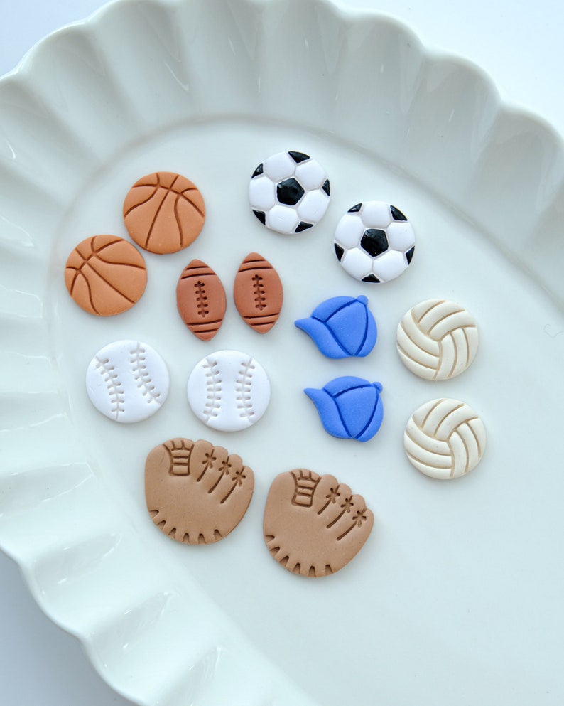Pu&ograve; includere: Una collezione di 12 orecchini in argilla colorata a forma di diverse attrezzature sportive, tra cui palline da baseball, palloni da basket, palloni da calcio, palloni da calcio, palloni da pallavolo e guanti da baseball.