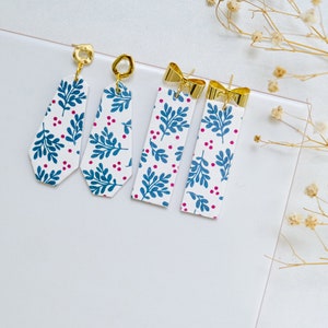 May include: Four pairs of dangle earrings with a white background and blue and pink floral pattern. The earrings have gold-colored hooks.