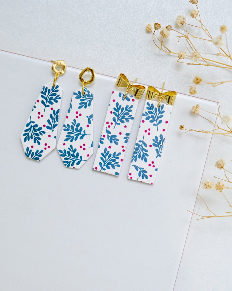 May include: Four pairs of dangle earrings with a white background and blue and pink floral pattern. The earrings have gold-colored hooks.