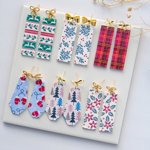 May include: Assortment of eight pairs of Christmas-themed earrings. The earrings are made of metal and feature various holiday patterns, including snowflakes, mittens, Christmas trees, and poinsettias. Each pair has a gold bow charm.
