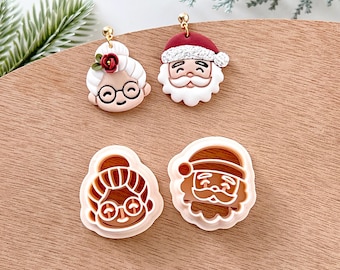 May include: Four Christmas-themed polymer clay earrings, two are finished and two are unfinished. The finished earrings are a Santa Claus and a woman with glasses and a red flower. The unfinished earrings are a Santa Claus and a woman with glasses.