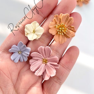 May include: Five polymer clay flower embellishments in various colors, including light blue, pink, white, and orange. Each flower has a gold center with small gold dots.