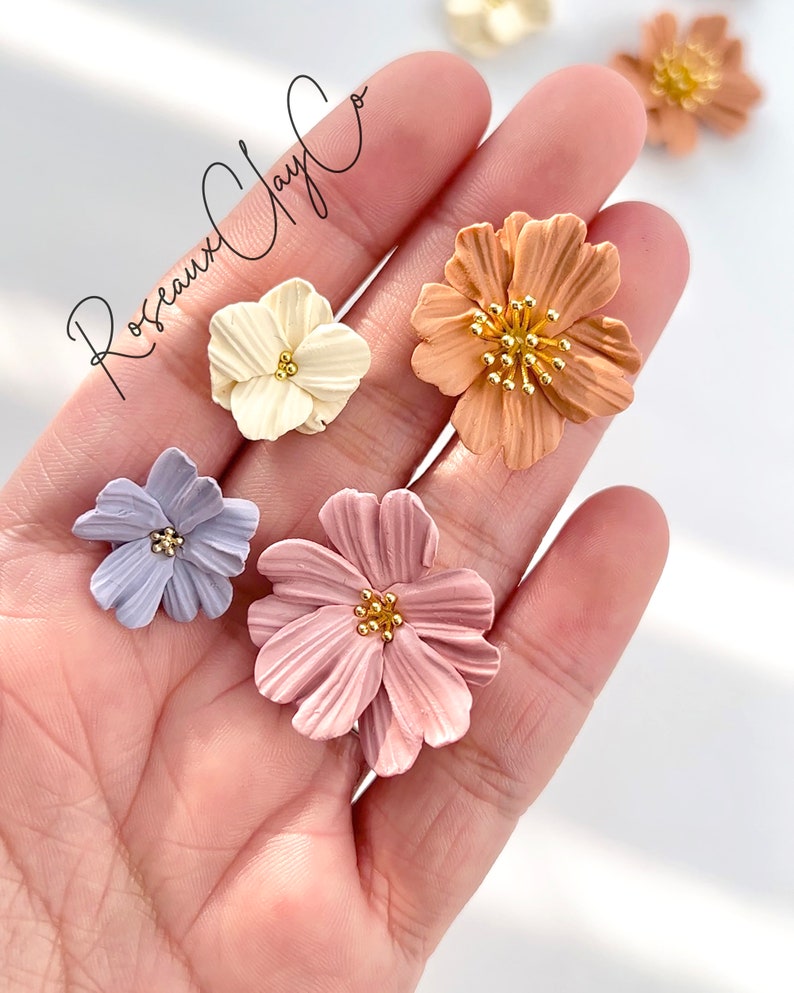 May include: Five polymer clay flower embellishments in various colors, including light blue, pink, white, and orange. Each flower has a gold center with small gold dots.
