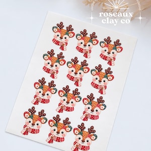 May include: A white rectangular sheet featuring eleven identical illustrations of a reindeer wearing a red and white plaid scarf. Each reindeer has brown antlers, a patchwork-style face in red, green, and tan, and a small button detail on the scarf.