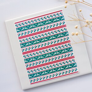 May include: White background with a sheet of wrapping paper featuring a repeating pattern of red berries, green holly leaves, white snowflakes, and teal reindeer.