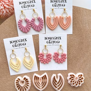 May include: A collection of polymer clay earrings in various shapes and colors, including pink, peach, and yellow. The earrings are displayed on white cards with the text "Roseaux Clayco." Also shown are clay cutters in matching designs.