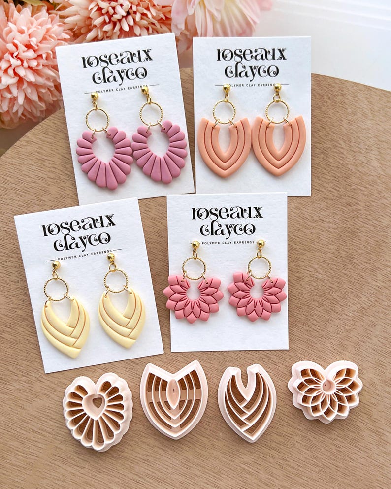 May include: A collection of polymer clay earrings in various shapes and colors, including pink, peach, and yellow. The earrings are displayed on white cards with the text "Roseaux Clayco." Also shown are clay cutters in matching designs.