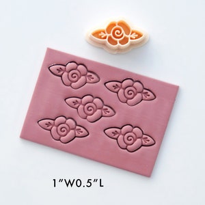May include: A pink silicone mold with five impressions of a rose design. The mold is 1 inch wide and 0.5 inches long. A single rose-shaped cookie cutter is shown above the mold.
