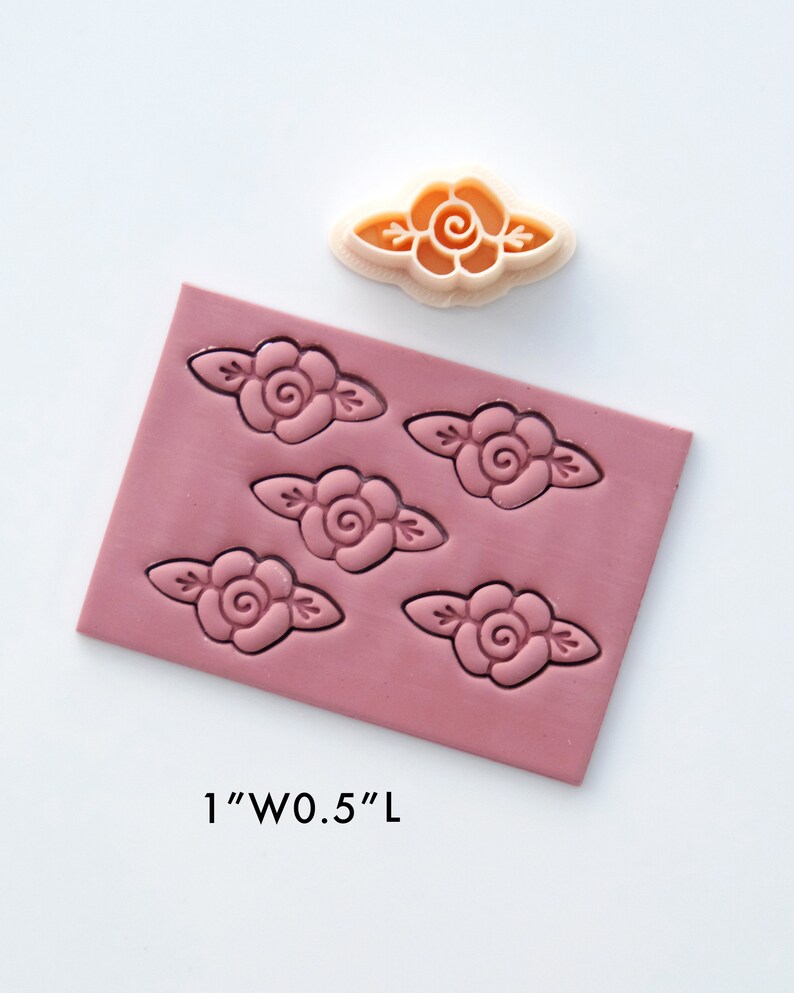 May include: A pink silicone mold with five impressions of a rose design. The mold is 1 inch wide and 0.5 inches long. A single rose-shaped cookie cutter is shown above the mold.