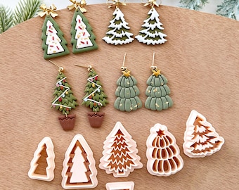 May include: A collection of Christmas-themed earrings and cookie cutters. The earrings feature green Christmas trees with gold bows, white accents, and colorful decorations. The cookie cutters are in the shape of Christmas trees and a flower pot.