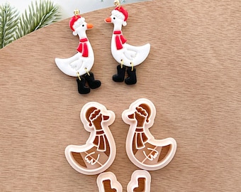 May include: A set of four white and brown goose-shaped Christmas earrings. The white geese are wearing red Santa hats and scarves. The brown geese are wearing brown scarves. The earrings are made of polymer clay and are perfect for adding a touch of whimsy to your holiday look.