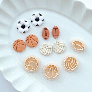 Pu&ograve; includere: Un piatto bianco con vari tagliapasta a tema sportivo. I tagliapasta sono a forma di pallacanestro, football americano, calcio e pallavolo.