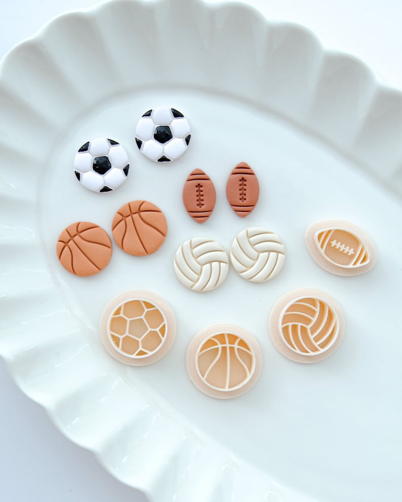 Pu&ograve; includere: Un piatto bianco con vari tagliapasta a tema sportivo. I tagliapasta sono a forma di pallacanestro, football americano, calcio e pallavolo.