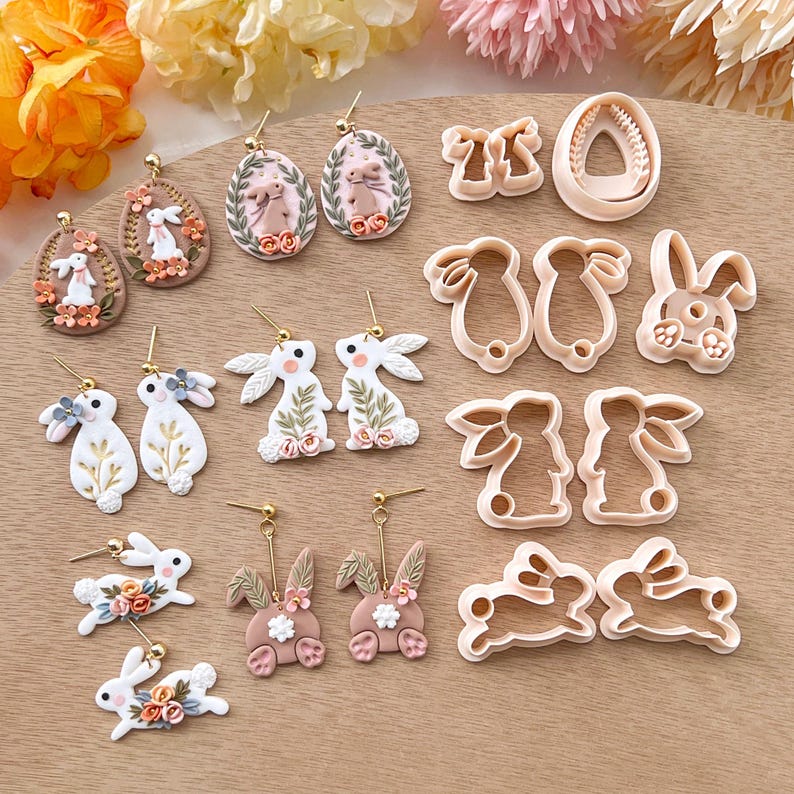 May include: A set of 10 polymer clay bunny and egg-shaped earrings and cookie cutters. The earrings are handmade and feature pastel pink, white, and gold accents. The cookie cutters are made of metal and are designed to cut out bunny and egg shapes.