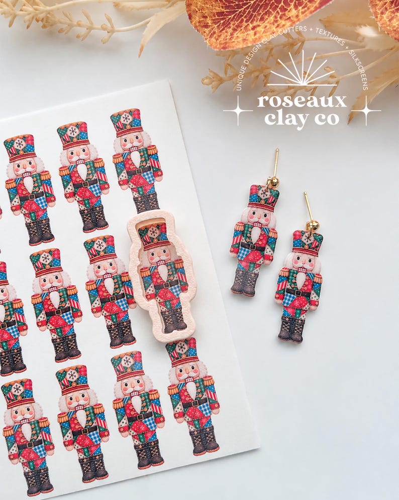 May include: A sheet of nutcracker-themed silkscreen transfers featuring multiple colorful nutcracker illustrations, a single beige nutcracker-shaped clay cutter, and a pair of dangling nutcracker earrings with gold-toned posts.