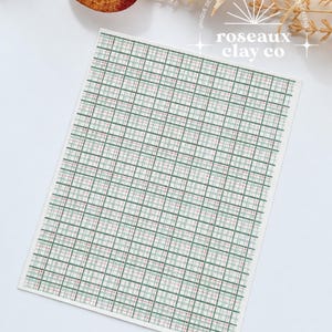 May include: A rectangular silkscreen sheet featuring a repeating plaid pattern in shades of sage green, white, and thin red lines. The top right corner displays the white text logo for roseaux clay co with a sunburst graphic above the brand name.