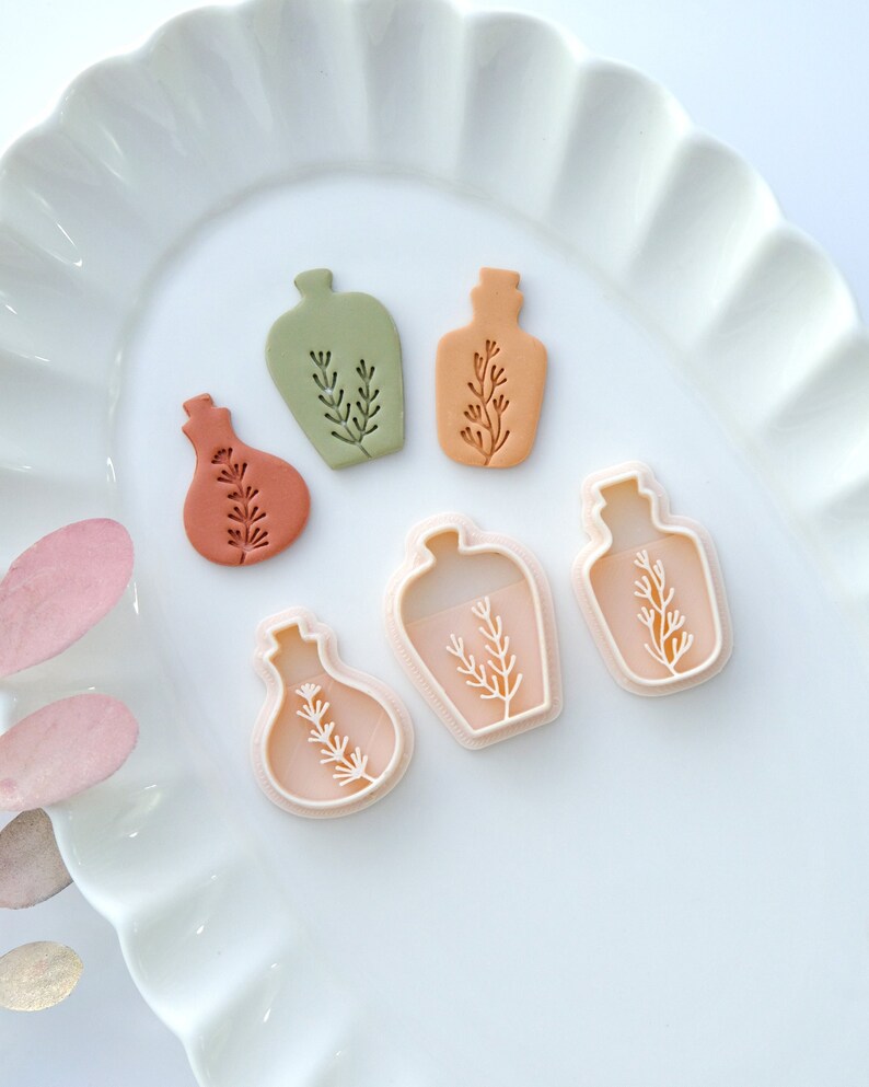 May include: Five cookie cutters in the shape of bottles with a sprig of leaves inside. The cutters are in various shades of green, orange, and brown.