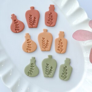 May include: Nine small ceramic bottles with a floral design in shades of orange, brown, and green. The bottles are arranged in three rows on a white plate.