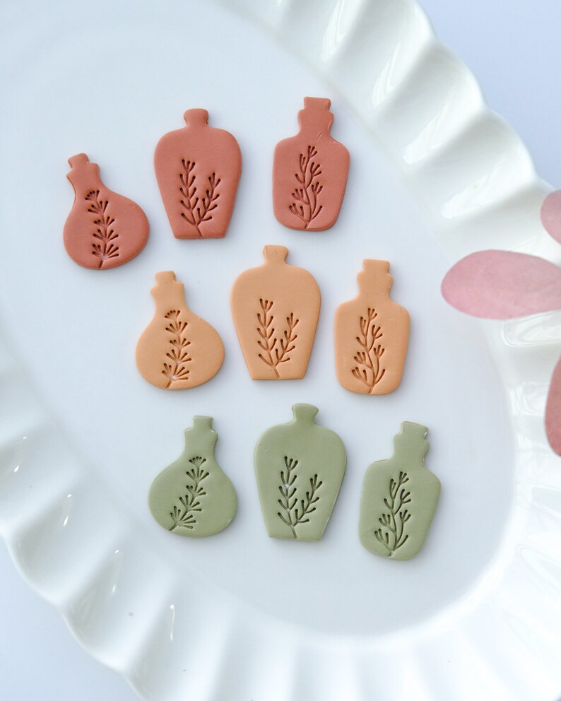 May include: Nine small ceramic bottles with a floral design in shades of orange, brown, and green. The bottles are arranged in three rows on a white plate.