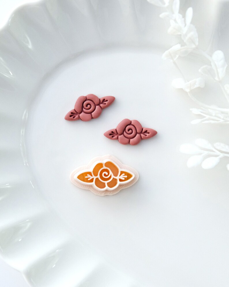 May include: Three resin rose flower embellishments in pink and orange. The roses are in a simple, classic style with a single swirl in the center and two leaves on either side.