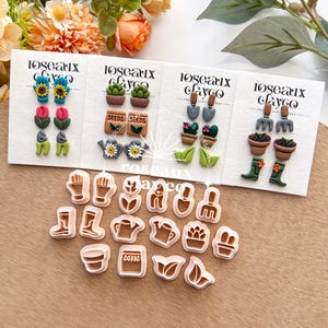 Könnte beinhalten: Ohrringe und Ausstecher aus Polymer Clay mit Gartenthema. Die Ohrringe zeigen Miniatur-Sonnenblumen, Tulpen und Gartengeräte. Die Ausstecher sind in Form von Gartengeräten und Pflanzen gestaltet, ideal zum Basteln. Die Ohrringe und Ausstecher sind auf weißen Karten ausgestellt.