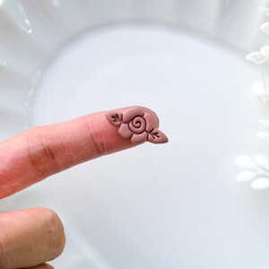 May include: A small, pink clay rose with leaves, perfect for adding a touch of charm to crafts and jewelry.