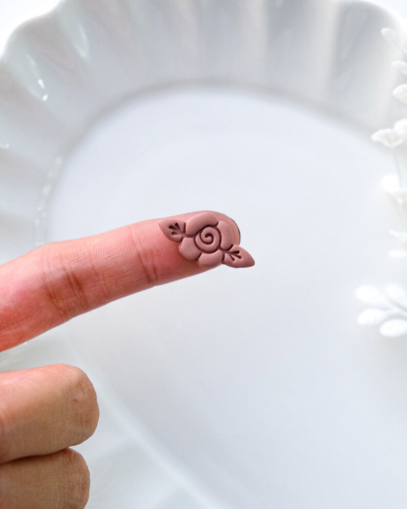 May include: A small, pink clay rose with leaves, perfect for adding a touch of charm to crafts and jewelry.
