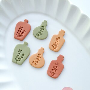 May include: Six small ceramic bottle ornaments in various shades of green, orange, and brown. Each bottle has a simple, stylized plant design.