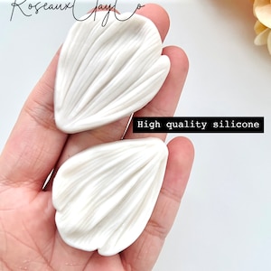 May include: Two white silicone molds for making flower petals. The molds are held in a hand. The text "High quality silicone" is visible in the image.