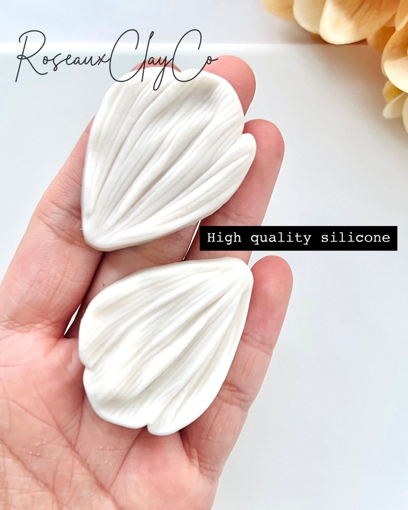 May include: Two white silicone molds for making flower petals. The molds are held in a hand. The text "High quality silicone" is visible in the image.
