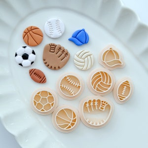 Pu&ograve; includere: Un set di 12 tagliapasta in plastica bianca e marrone a forma di varie attrezzature sportive, tra cui palline da baseball, palloni da basket, palloni da calcio, palloni da calcio, palloni da pallavolo e un guanto da baseball.
