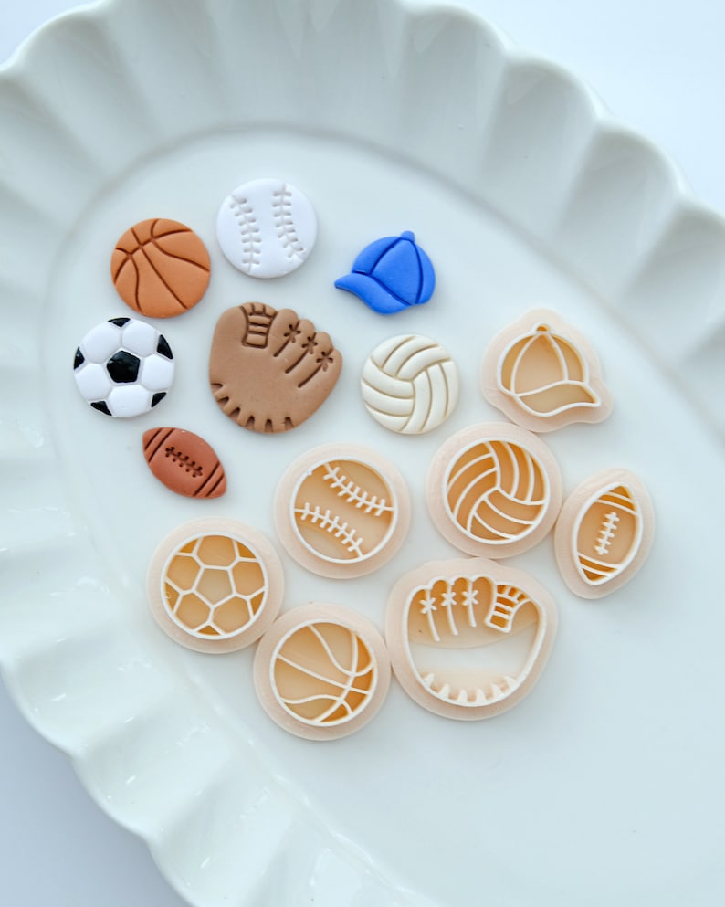 Pu&ograve; includere: Un set di 12 tagliapasta in plastica bianca e marrone a forma di varie attrezzature sportive, tra cui palline da baseball, palloni da basket, palloni da calcio, palloni da calcio, palloni da pallavolo e un guanto da baseball.