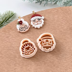 May include: A set of four Christmas cookie cutters featuring Santa Claus and Mrs. Claus. The cutters are made of a light pink plastic and are ready to use for holiday baking.