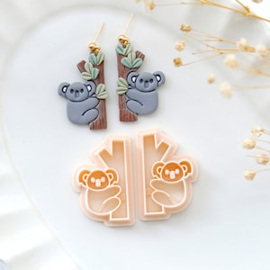 May include: A pair of gray koala earrings with brown branches and green leaves, and a matching pair of koala cookie cutters.