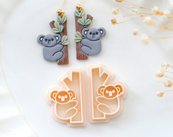 May include: A pair of gray koala earrings with brown branches and green leaves, and a matching pair of koala cookie cutters.